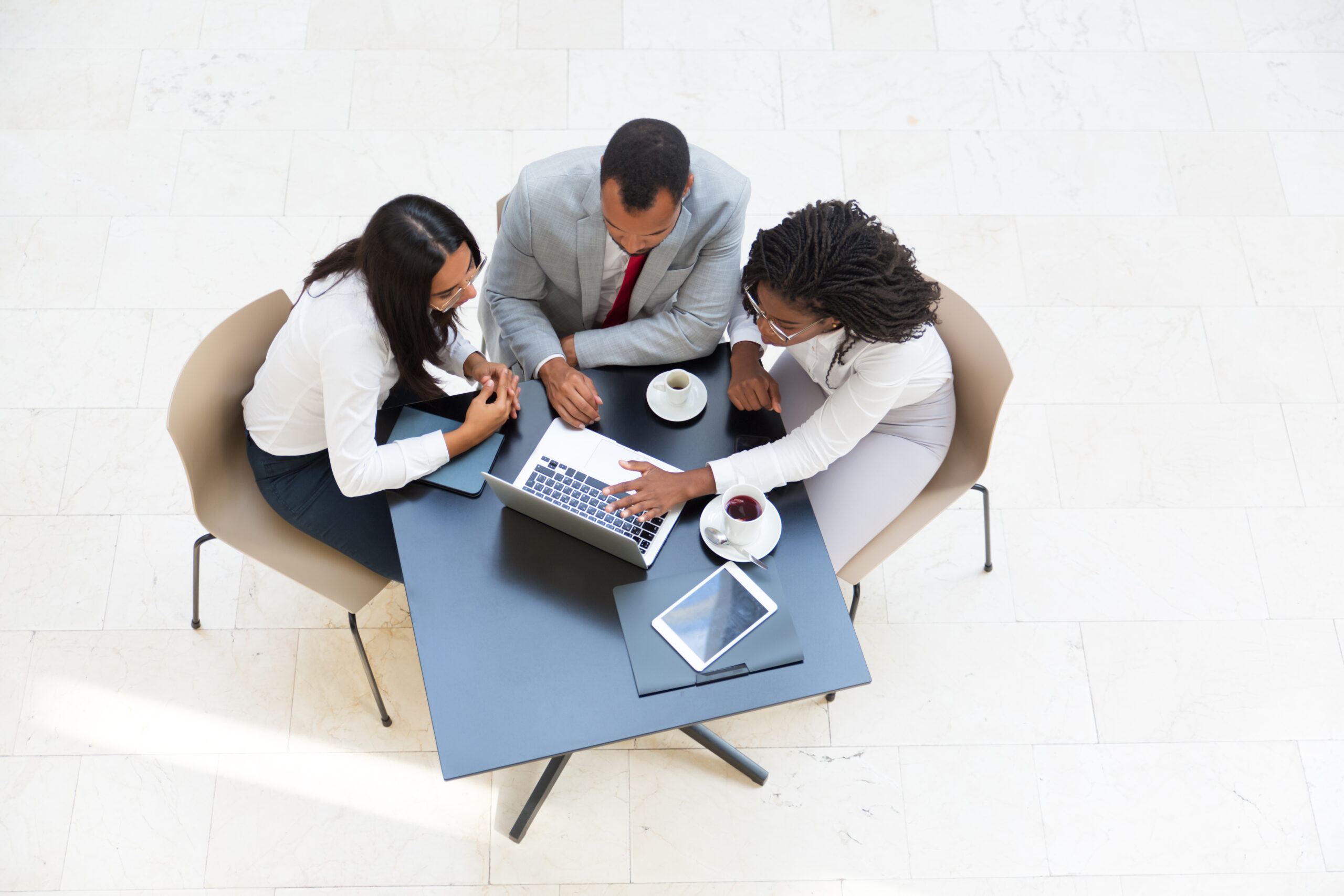 Business colleagues watching content on laptop while drinking coffee. Business man and women sitting at table with tablet, working on computer, looking at screen. Wireless communication concept
